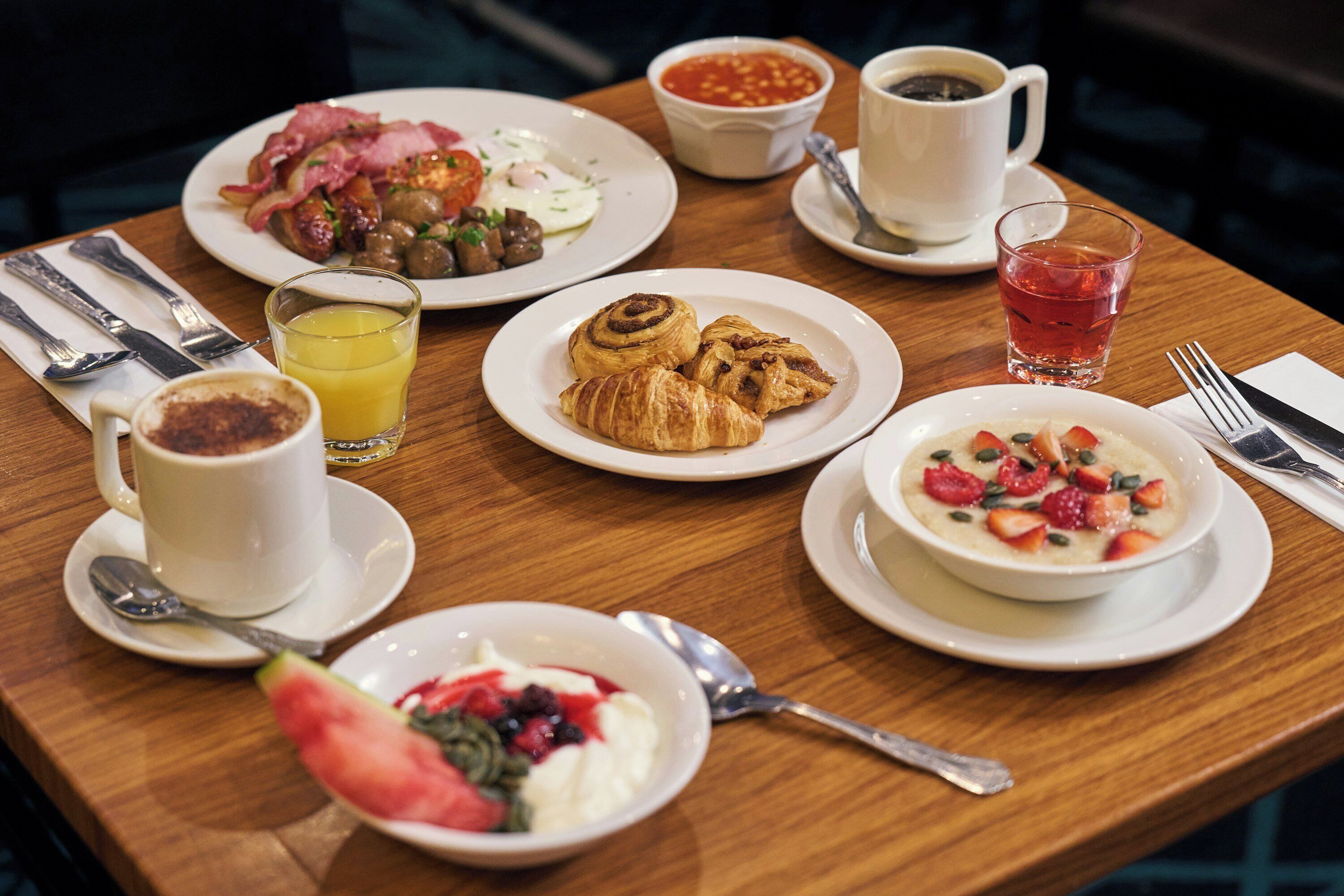 A breakfast table with plates of food, a cup of coffee, a glass of juice, and a bowl of fruit salad.