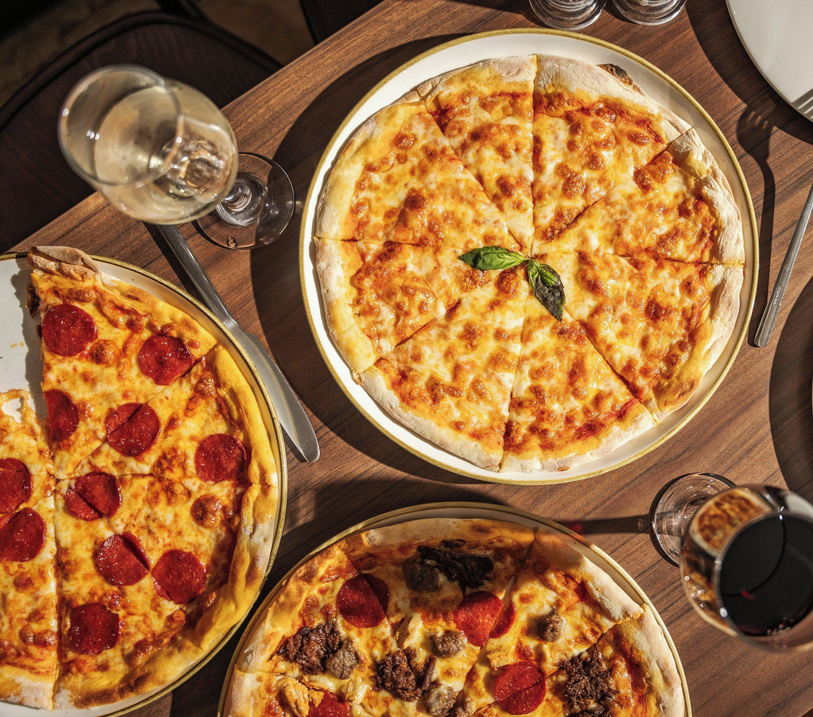 Drei Pizzen auf einem Holztisch mit Gläsern und Besteck.