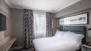 A modern hotel room with a large bed, a flat-screen TV, a nightstand, and a cityscape artwork on the wall.