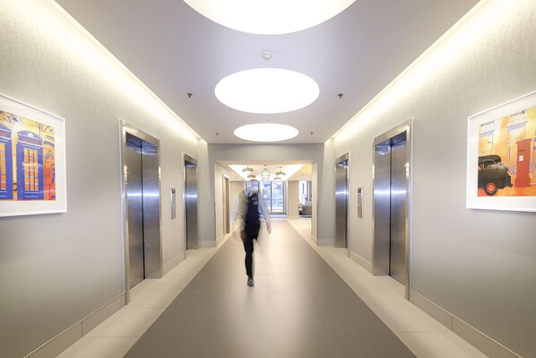 En moderne hotelgang med elevatorer, indbygget lys og kunst på væggene.