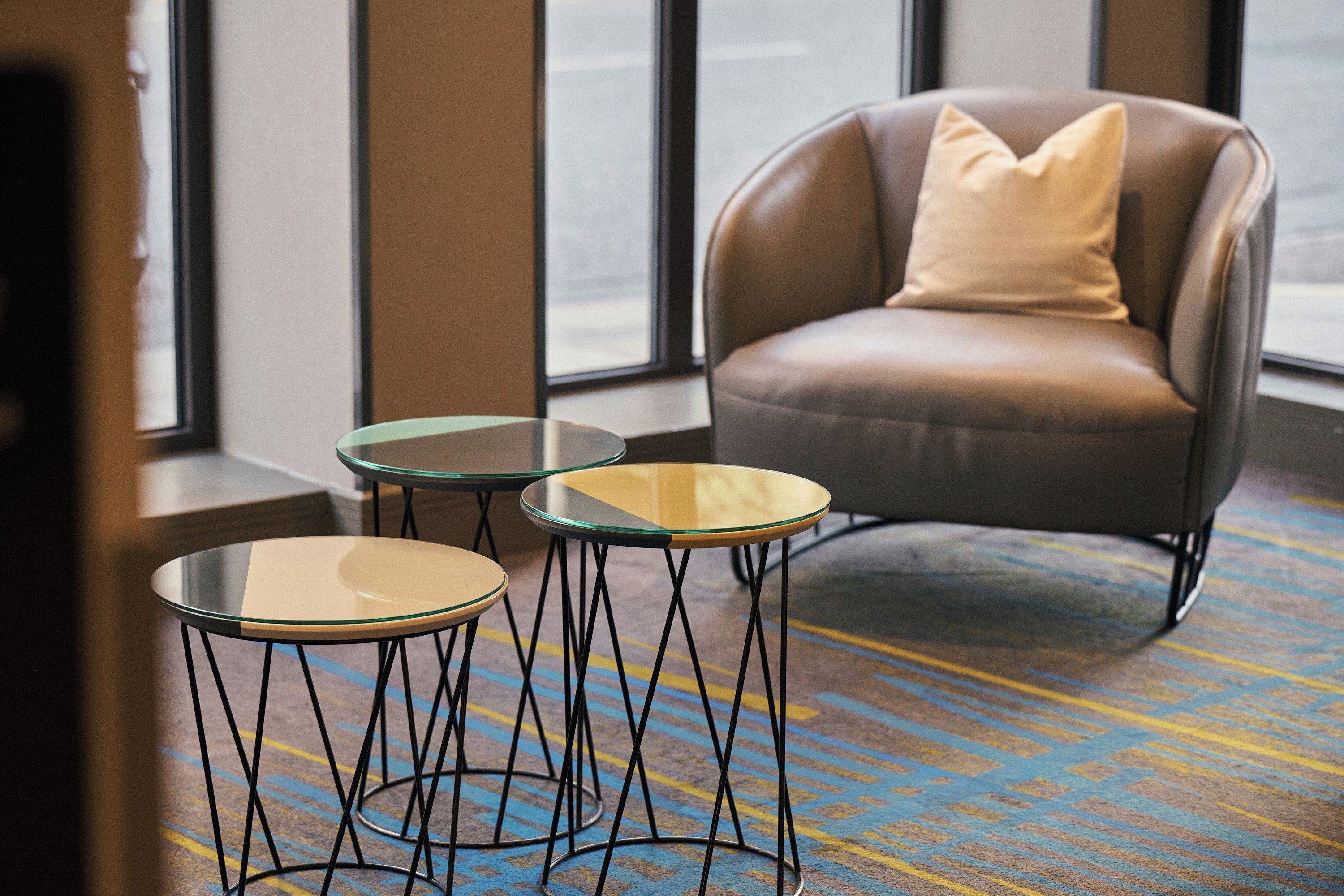 A room with a brown leather armchair, two glass-top tables with black metal legs, and a patterned carpet.