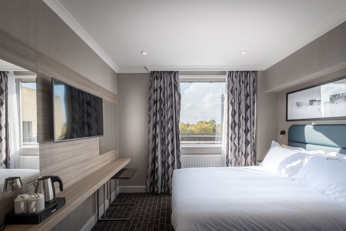 Ein modernes Hotelzimmer mit einem großen Bett, einem Flachbildfernseher, einer Kaffeemaschine und Blick auf die Stadt.