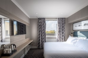 Ein modernes Hotelzimmer mit einem großen Bett, einem Flachbildfernseher, einer Kaffeemaschine und Blick auf die Stadt.