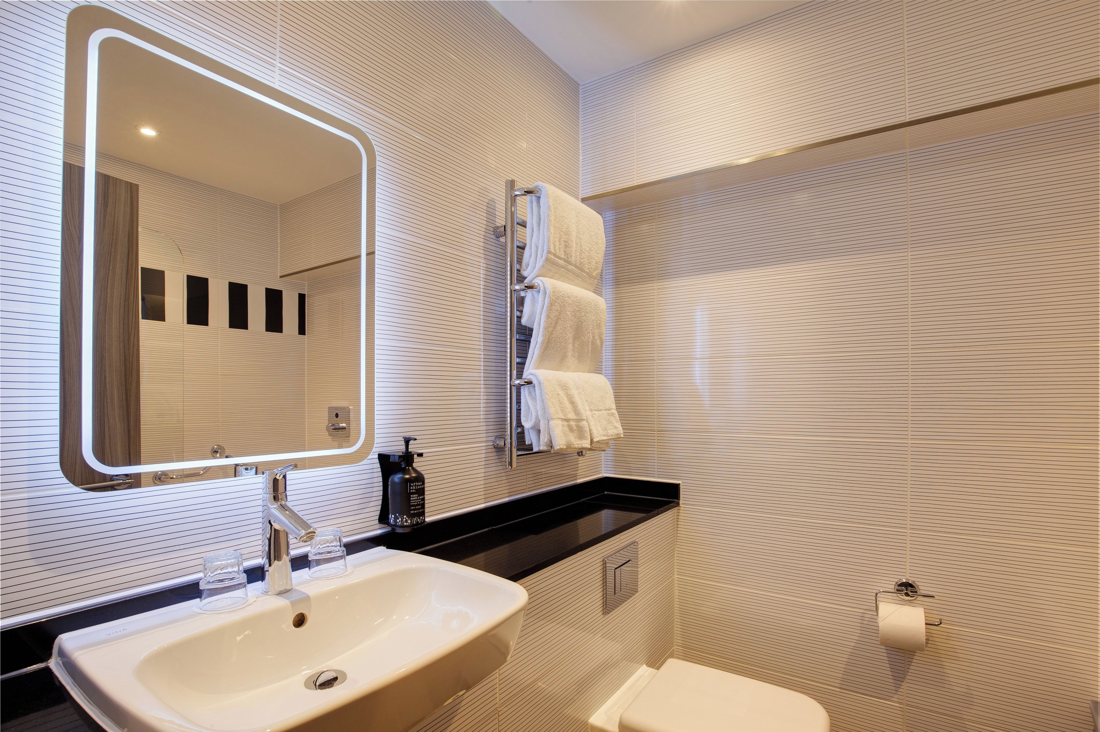 A modern bathroom with a large mirror, a sink, a towel rack, and a toilet.