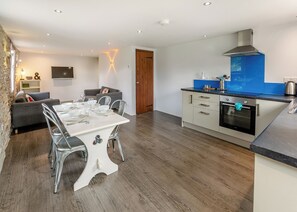 A modern kitchen with a built-in oven, a blue backsplash, and a dining area with a white table and metal chairs.