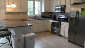 Une cuisine moderne avec des meubles blancs, des appareils en acier inoxydable, un plan de travail en granit et deux poubelles.