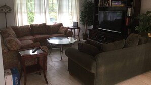 Un salon comprenant un canapé, une table basse, un meuble pour la télévision et un ventilateur de plafond.