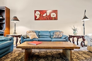 A living room with a blue sofa, a wooden coffee table, and a red book on it. - Upscale Condo | Min from Shopping and Restaurants (Mesa)