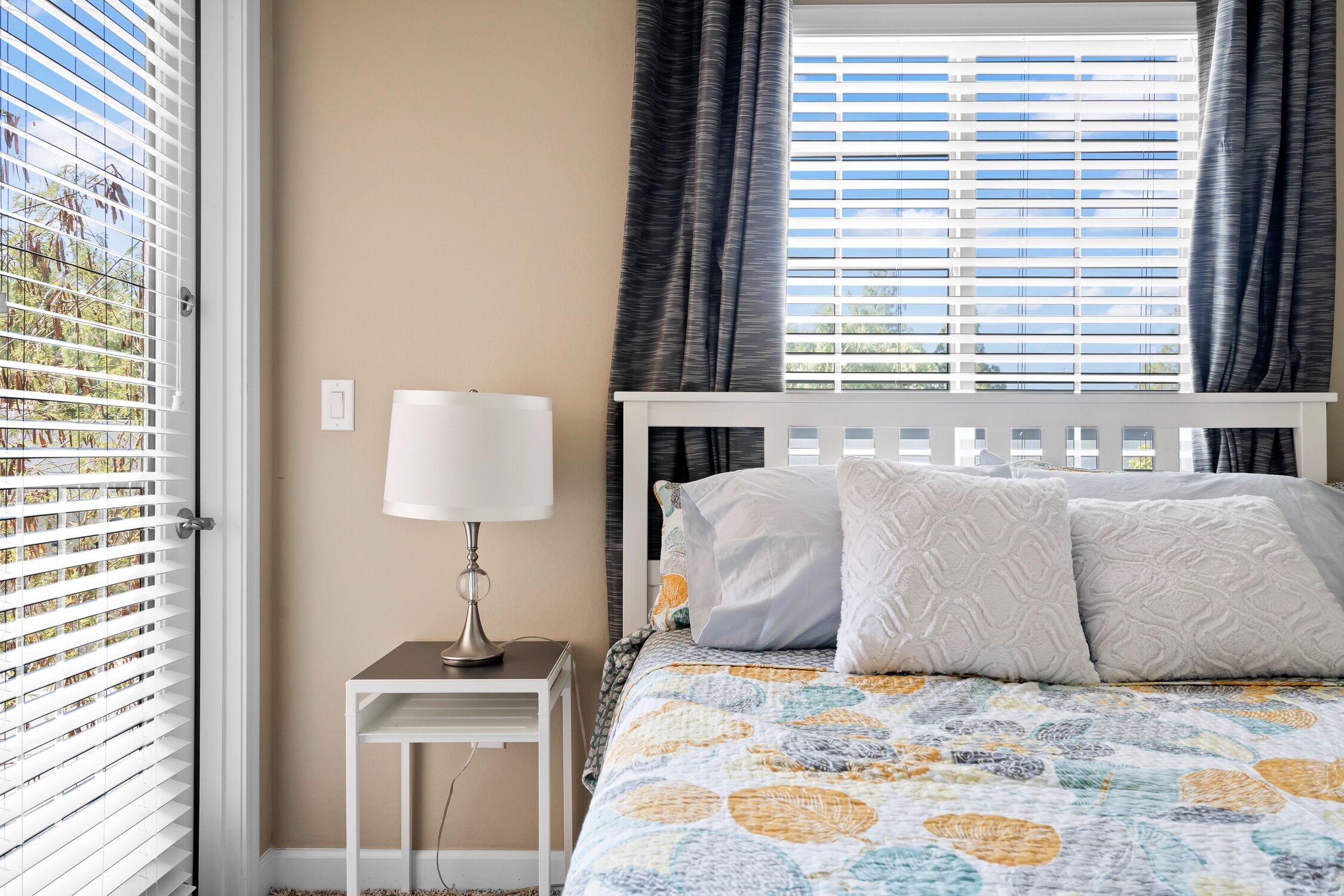 A bedroom with a bed, a bedside table with a lamp, and a window with blinds.