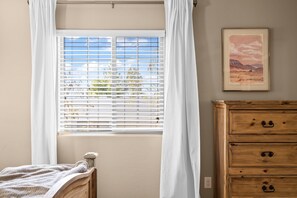 Un dormitorio con cama, cómoda de madera, ventana con persianas y un cuadro en la pared.
