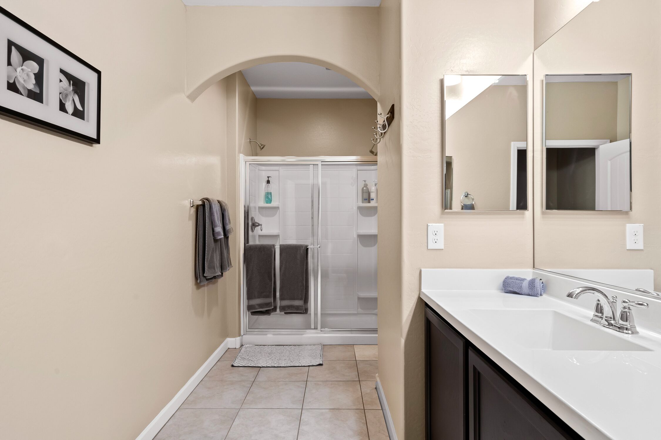 A modern bathroom with a large mirror, a shower with glass doors, and a white sink.