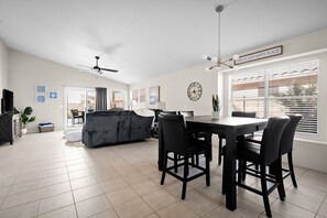 A spacious living area with a dining table, black chairs, a grey sofa, and a ceiling fan.