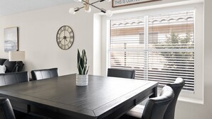 A dining area with a dark wooden table, black chairs, a potted plant, a wall clock, and a window with blinds. - Sunny Peoria Escape w/ Private Pool + Fire Pit (Peoria)