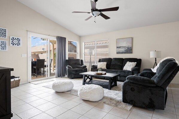 A spacious living room with a ceiling fan, a sofa set, ottomans, and a coffee table.