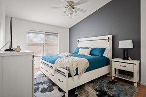A bedroom with a bed, bedside table, lamp, and a ceiling fan.