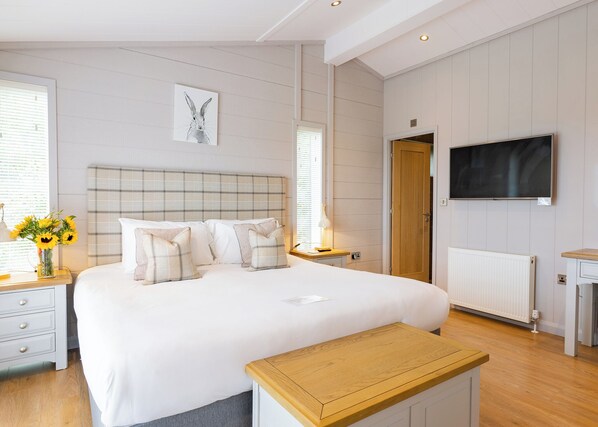 A bedroom with a bed, bedside tables, a TV, and a window with blinds.