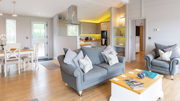 A modern living room with a grey sofa, a wooden coffee table, and a dining area with white furniture. - 2 bedroom accommodation in Cannington (Cannington)