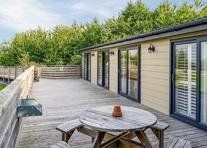 A wooden deck with a round table and benches, a glass door entrance, and a wooden fence.