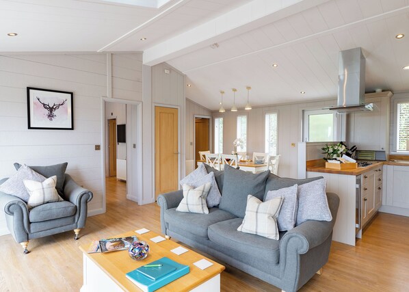 A spacious living area with a grey sofa, a wooden coffee table, and a dining table with chairs.