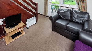 Una sala de estar con un televisor sobre un mueble de madera, un sofá de cuero negro, un radiador y una escalera.