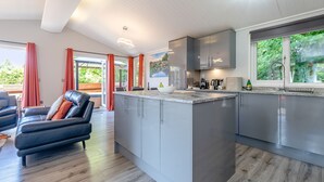 A modern kitchen with grey cabinets, a central island, and a dining area with a black leather sofa. - Bakewell Deluxe Lodge (Longnor, Nr. Buxton)