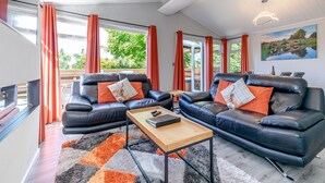 A modern living room with two black leather sofas, a wooden coffee table, and a large window with curtains. - Bakewell Deluxe Lodge (Longnor, Nr. Buxton)
