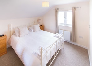 Quarto com uma cama de solteiro, mesa de cabeceira, abajur, janela com cortinas e radiador.