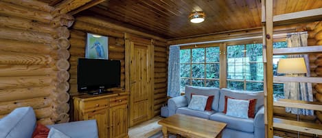 A log cabin interior with a sofa, television, and a window with a view of greenery.