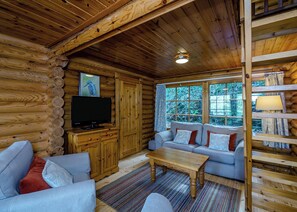 A log cabin interior with a sofa, television, and a window with a view of greenery.