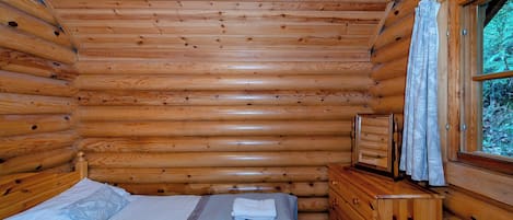 Una habitació de cabana de fusta amb un llit, una petita còmoda i una finestra amb cortines.