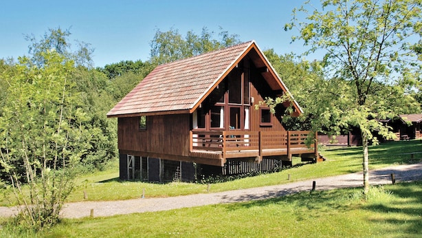 A wooden cabin with a sloped roof, a balcony, and a surrounding grassy area. - Single storey A-frame lodge. (North Tamerton, Bude)