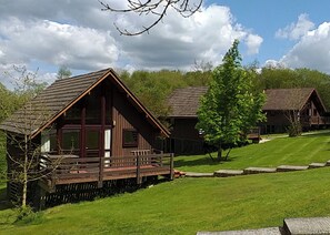Eine Reihe von Holzhütten mit einer Terrasse, umgeben von einer Rasenfläche und Bäumen.