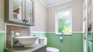 Un bany amb un lavabo blanc, un vàter, una finestra amb vistes i un mirall sobre el lavabo.