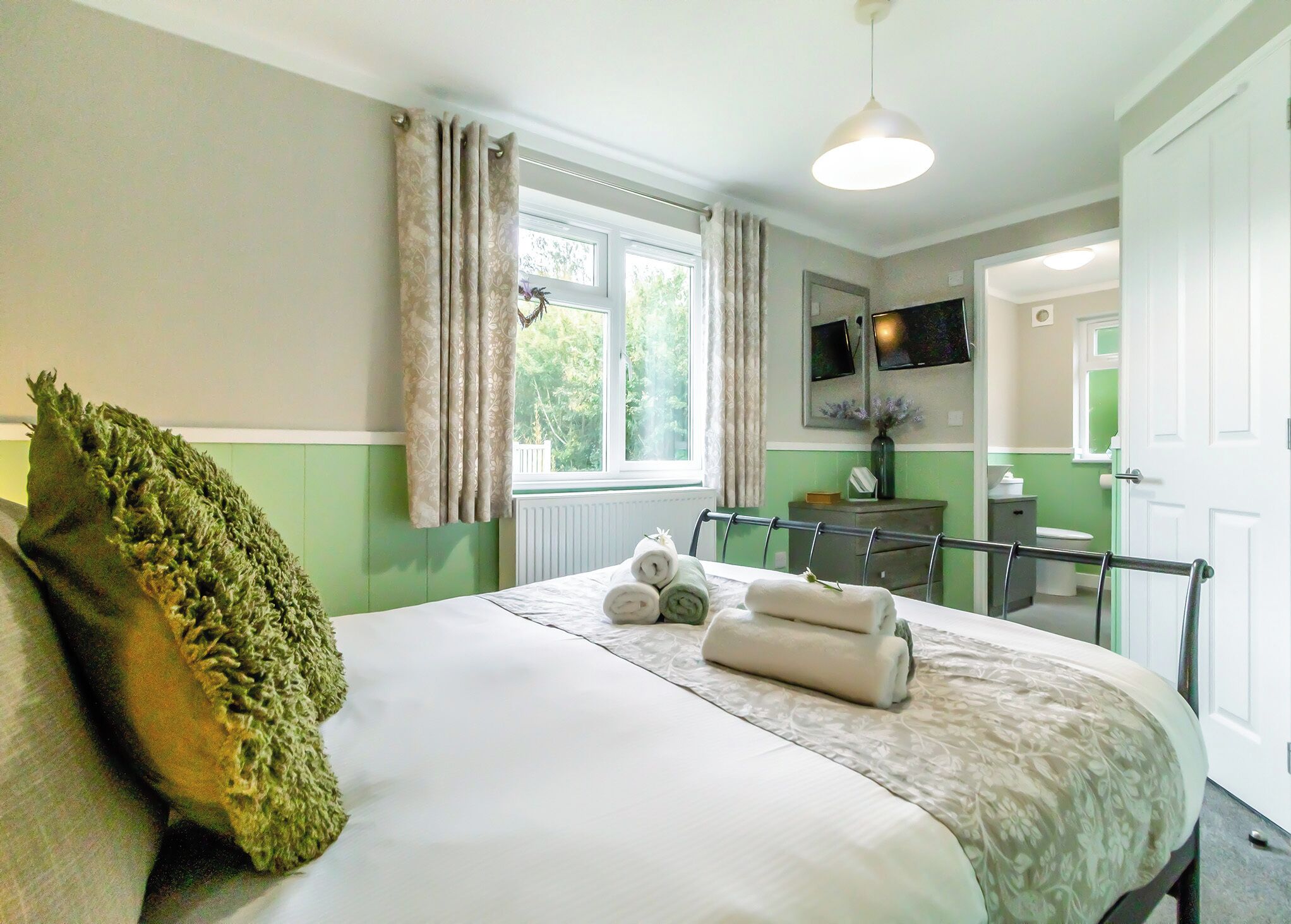 Une chambre à coucher avec un lit, une fenêtre avec des rideaux, une table de chevet avec une lampe et un miroir.