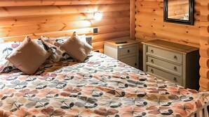 Ein Schlafzimmer einer Holzhütte mit einem Bett, Kissen, einem Nachttisch, einer Kommode und einem Spiegel.