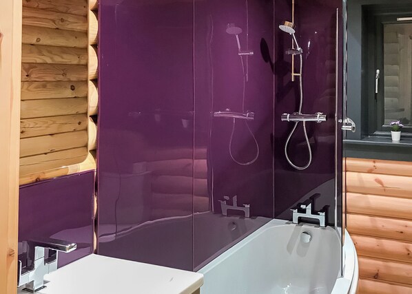 A modern bathroom with a glass-enclosed shower, a white bathtub, and wooden paneling on the walls.