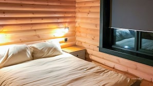 Ein Zimmer in einer Holzhütte mit einem Bett, einem Nachttisch und einem Fenster.