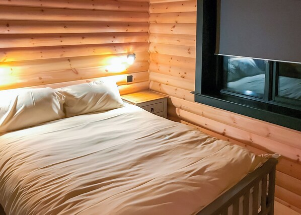 Una habitación de cabaña de madera con una cama, mesita de noche y ventana.