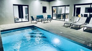 En swimmingpool med liggestole og en glasdør, der fører til et rum.