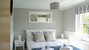 Un dormitorio con cama, mesitas de noche, un espejo y una ventana con cortinas.