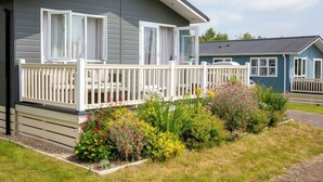 Una casa móvil de un piso con balcón, rodeada por un jardín con diversas plantas y flores.