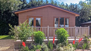 Un piccolo chalet in legno con un patio, circondato da un giardino con diverse piante e fiori.