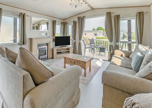 A spacious living room with a fireplace, a flat-screen TV, and a balcony with outdoor furniture. - Luxurious 14ft-wide holiday home. (Looe)