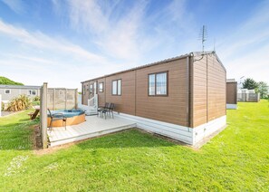 A single-story mobile home with a deck, a hot tub, and a small patio area. - Luxurious 14ft-wide holiday home. (Looe)