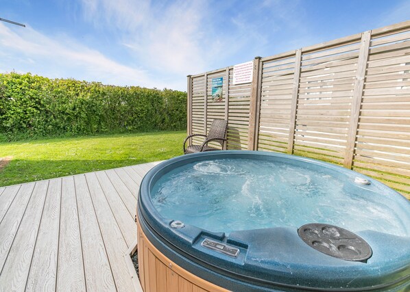 Ein Whirlpool auf einer Holzterrasse mit Holzzaun und Hecke im Hintergrund.