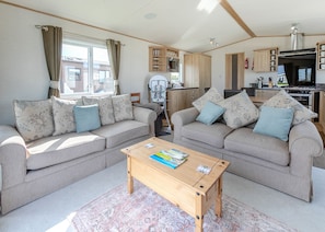 A living room with two sofas, a coffee table, and a kitchen area with cabinets and appliances. - Luxurious 14ft-wide holiday home. (Looe)