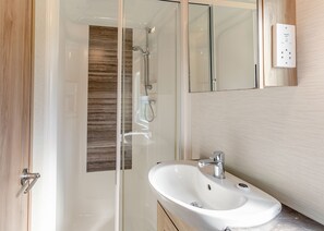 Ein modernes Badezimmer mit einer begehbaren Glasdusche, einem weißen Waschbecken und einem Spiegel.