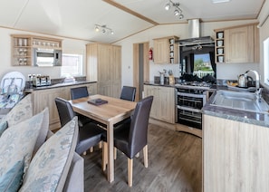 A compact kitchen with a dining area, wooden cabinets, a microwave, stove, and a sink. - Luxurious 14ft-wide holiday home. (Looe)