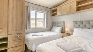 Une chambre avec deux lits, des armoires en bois, une fenêtre avec des rideaux, une lampe de chevet et une tête de lit capitonnée.