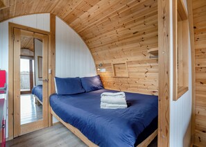 A bedroom with a curved ceiling, wooden walls, a bed with blue bedding, and a small window. - 0 bedroom accommodation in Great Busby (Great Busby)